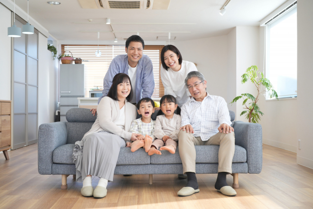 alt="新しい家のリビングで三世代の家族が笑顔で並んでいる写真。ファイブイズホームで費用を抑えながら安心して暮らすイメージを表現している。"